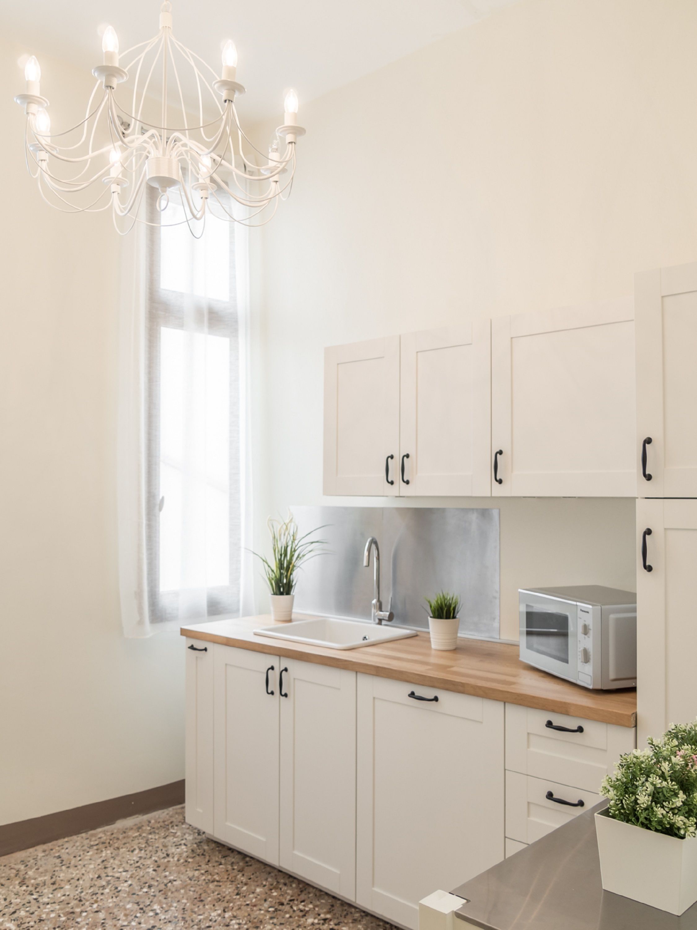 Una cucina moderna con mobili bianchi, un piano di lavoro in legno, un lavello, un forno a microonde e un lampadario.