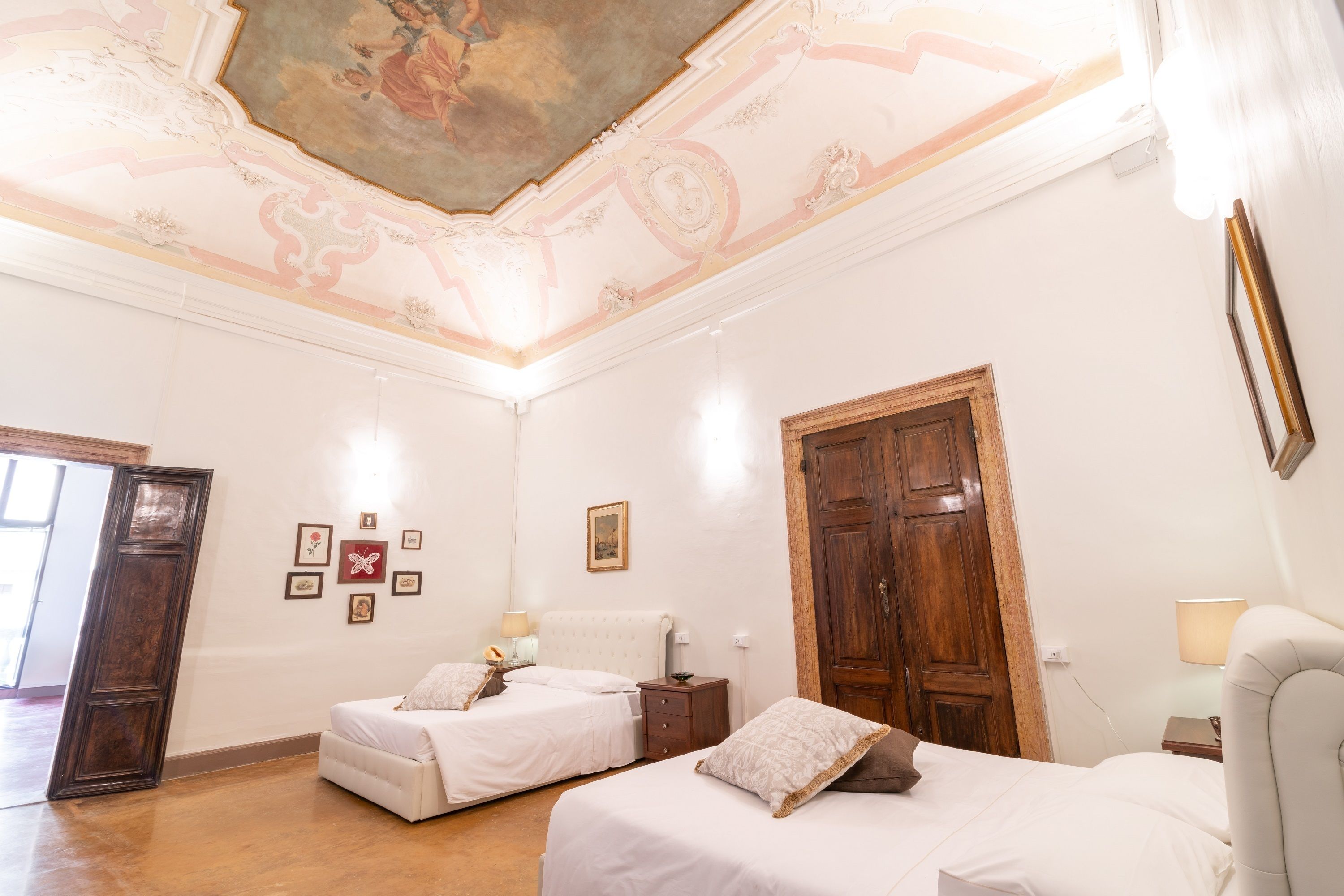 A room with two beds, a wooden door, and a ceiling with decorative artwork.