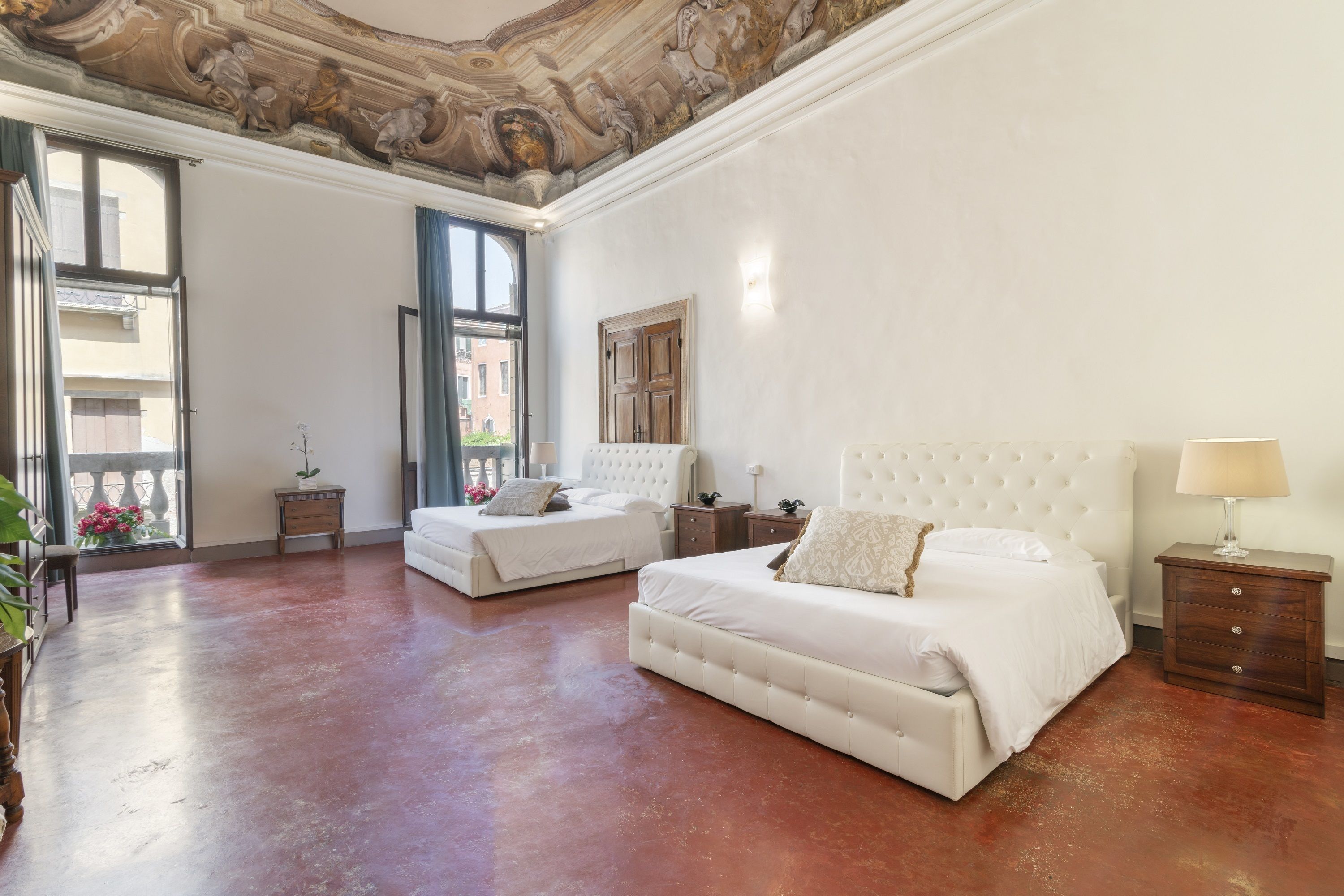 A spacious bedroom with two beds, a large window, and a decorative ceiling.