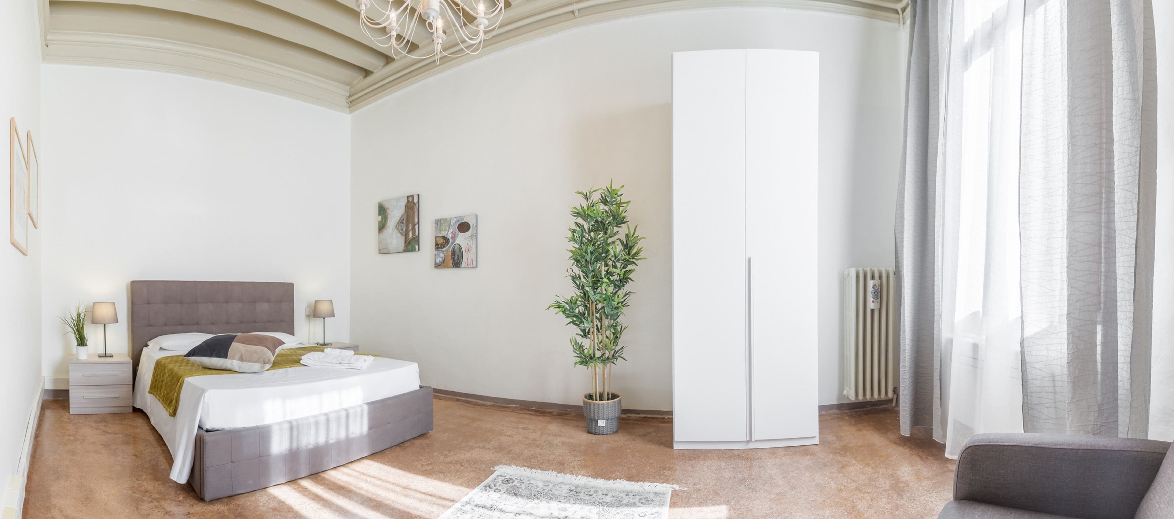 A modern bedroom with a bed, bedside tables, a potted plant, a wardrobe, and a radiator.