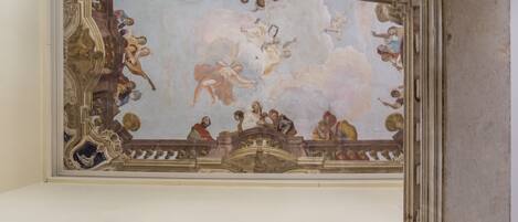 A ceiling with a classical fresco mural, ornate moldings, and a decorative cornice.