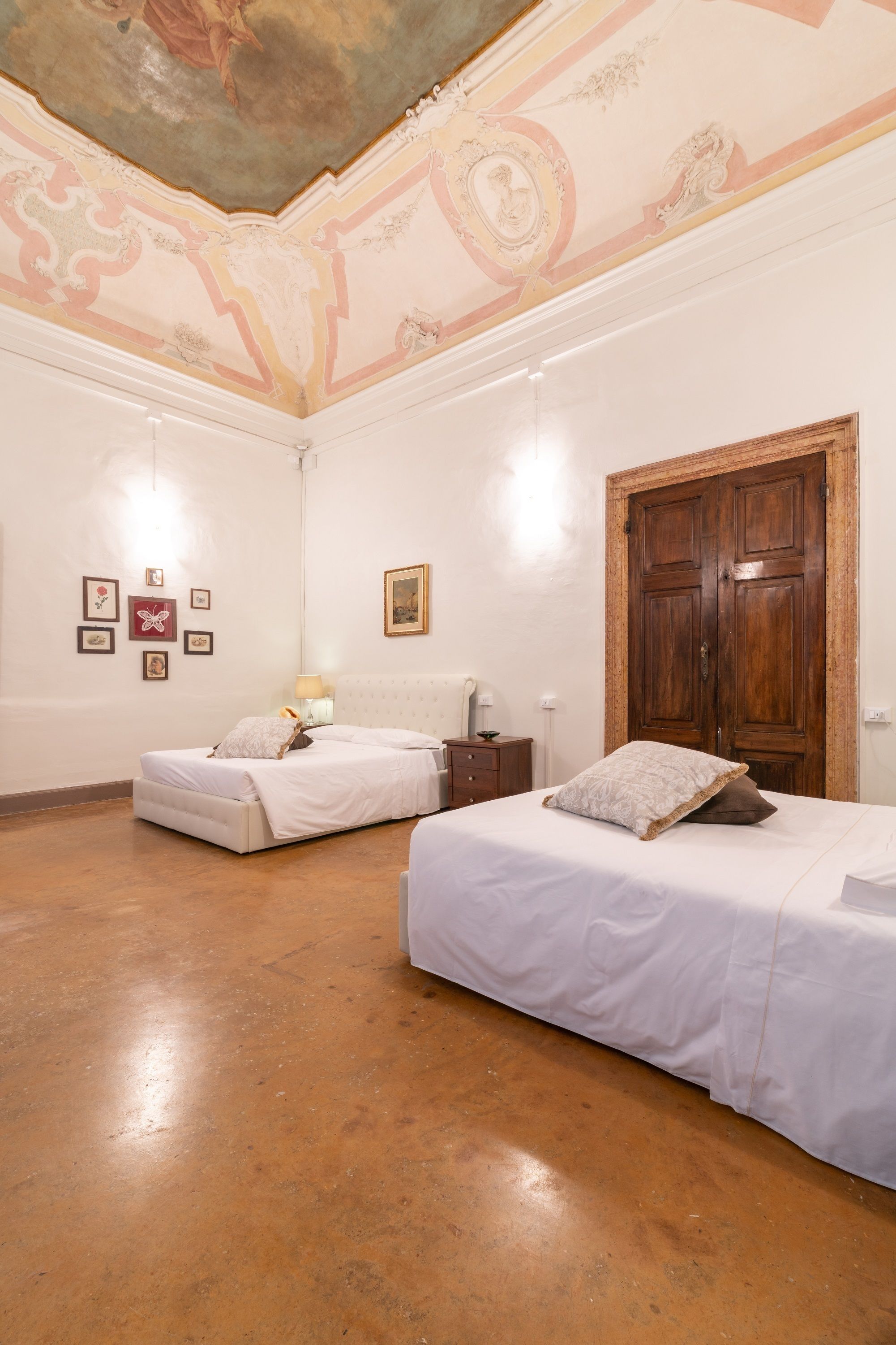 A room with two beds, a wooden wardrobe, and a ceiling with decorative frescoes.