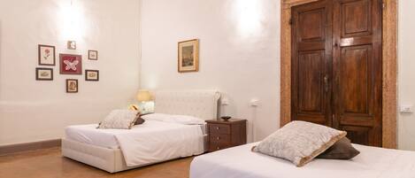 A room with two beds, a wooden wardrobe, and a ceiling with decorative frescoes.