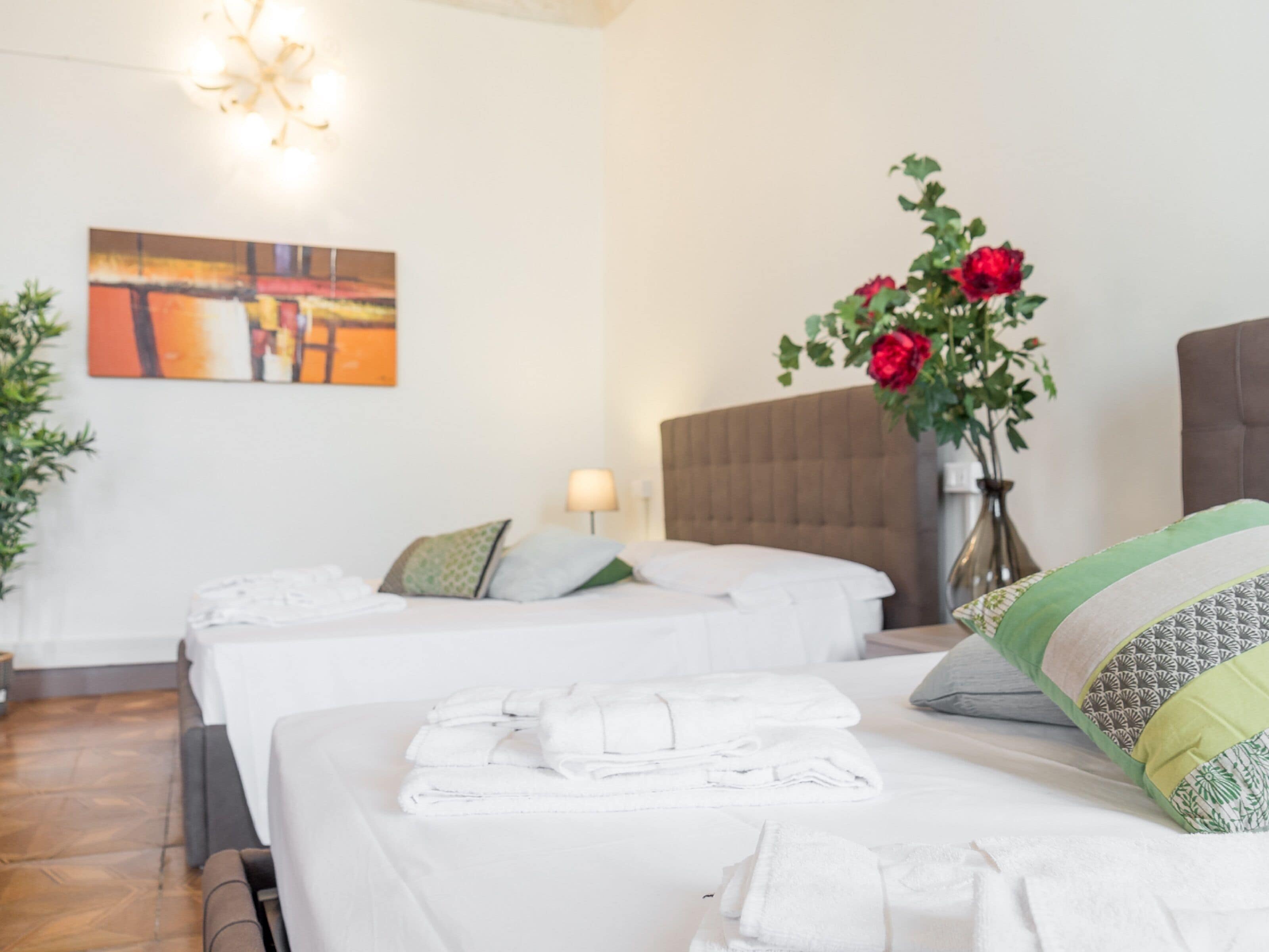 Una habitació d'hotel amb dos llits, un quadre gran a la paret, un ram de flors vermelles i una làmpada.