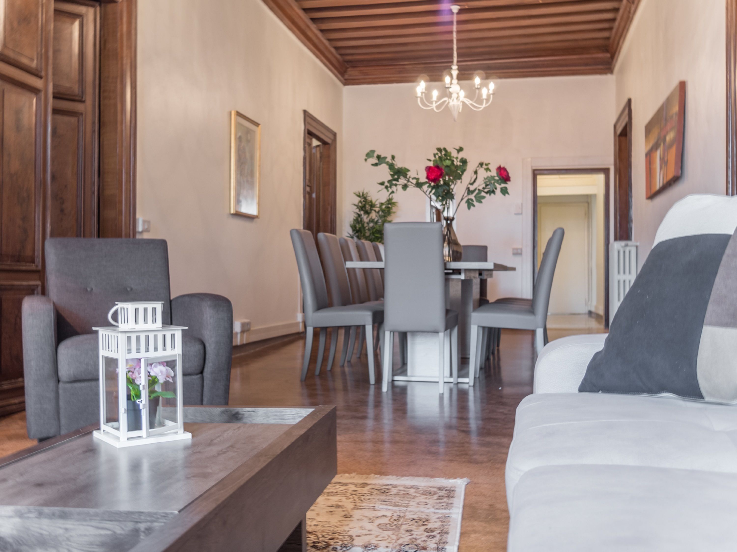 A spacious living room with a wooden ceiling, a dining area with a table and chairs, and a sofa.