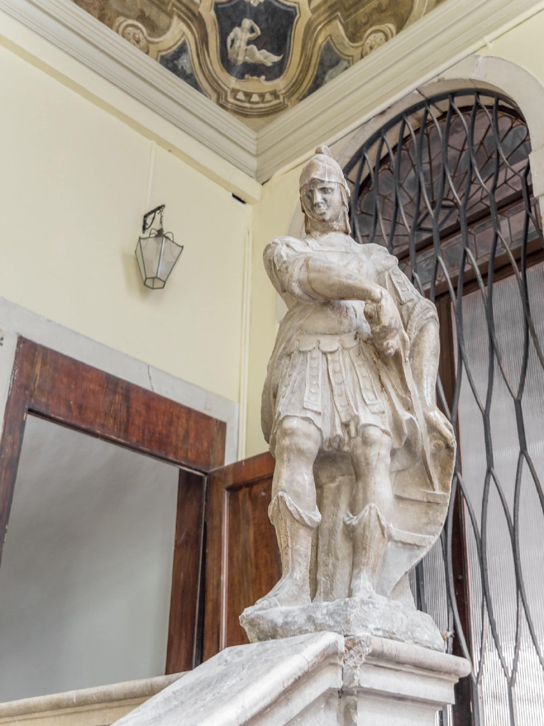 A statue of a historical figure in a room with a decorative ceiling and a metal gate.