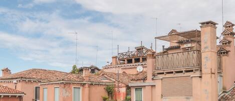 A row of traditional buildings with terracotta roofs and green shutters, featuring a mix of balconies and windows.