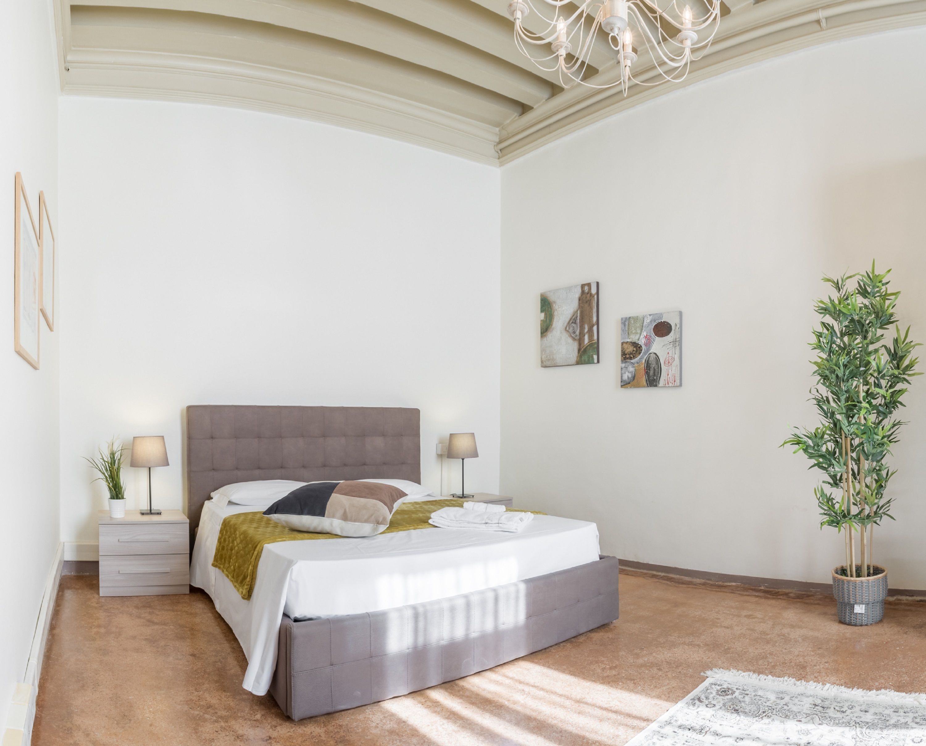 Un dormitorio con una cama grande, dos mesitas de noche, un candelabro y una planta en maceta.