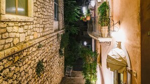 A narrow stone pathway leading to a building with a stone facade and a balcony with potted plants. - Casa Turchetti - Taormina (Taormina)