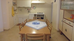 A compact kitchen with a dining table, chairs, cabinets, and a stove. - Casa Cairo Affittacamere (Mombaroccio)
