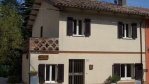 A two-story building with a tiled roof, a brick section on the ground floor, and shutters on the windows. - Casa Cairo Affittacamere (Mombaroccio)