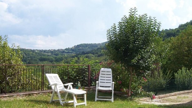 Two white lounge chairs and a small table on a grassy lawn with a view of a hilly landscape. - Casa Cairo Affittacamere (Mombaroccio)