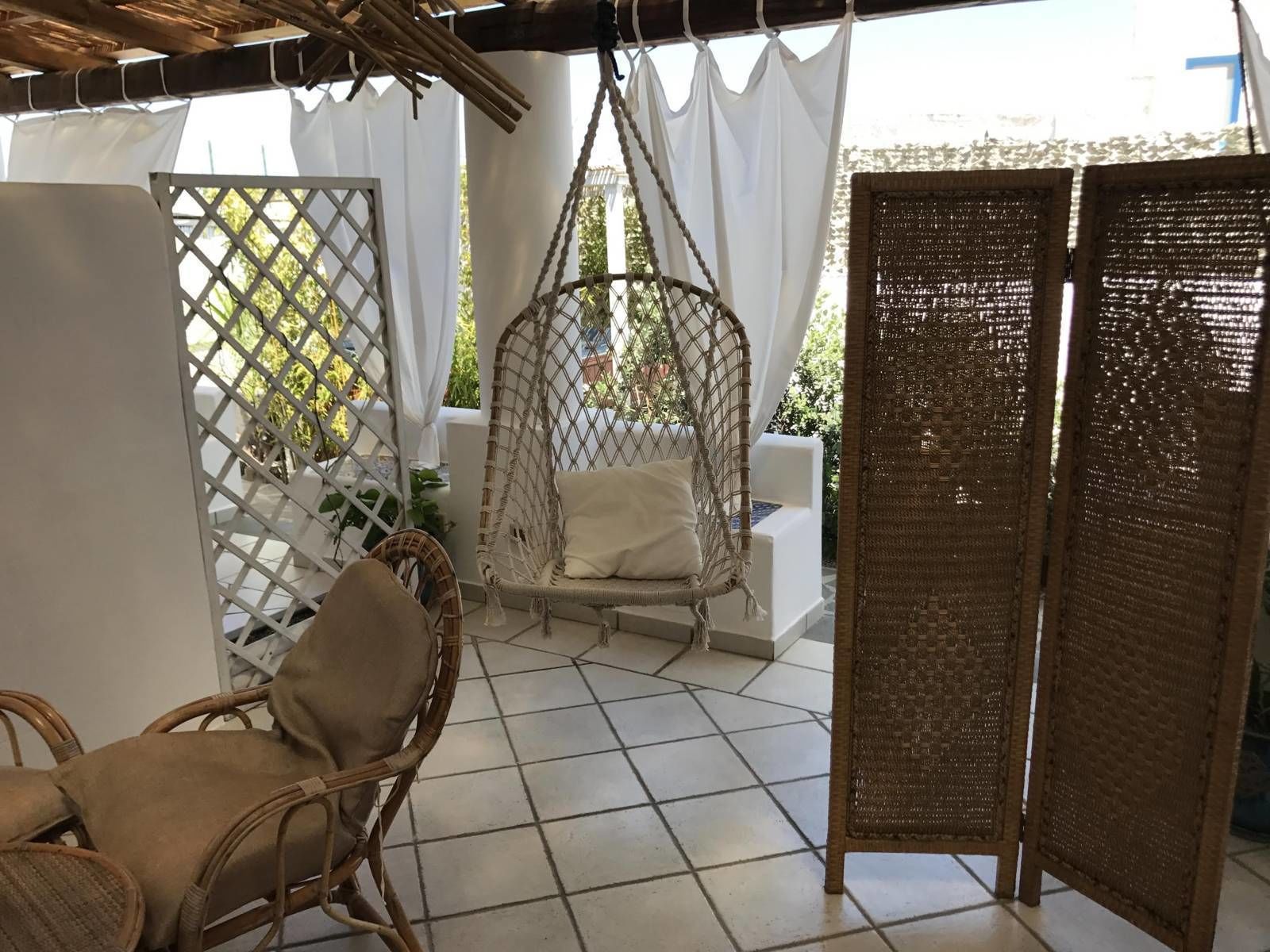 A patio area with a hanging chair, a wicker chair, and a woven partition.
