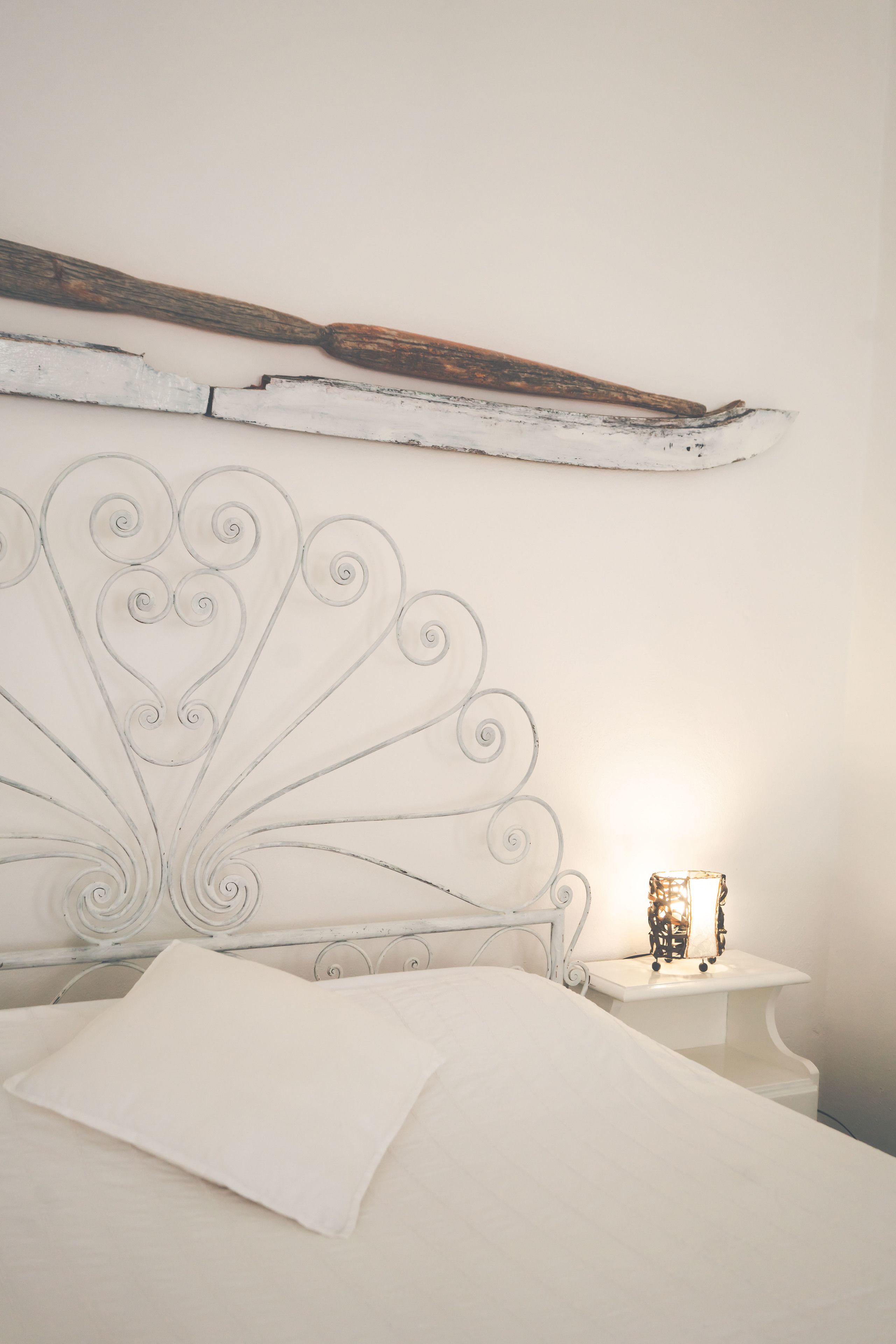 A bed with a white headboard, a bedside table with a small lamp, and a rustic wooden beam above the bed.