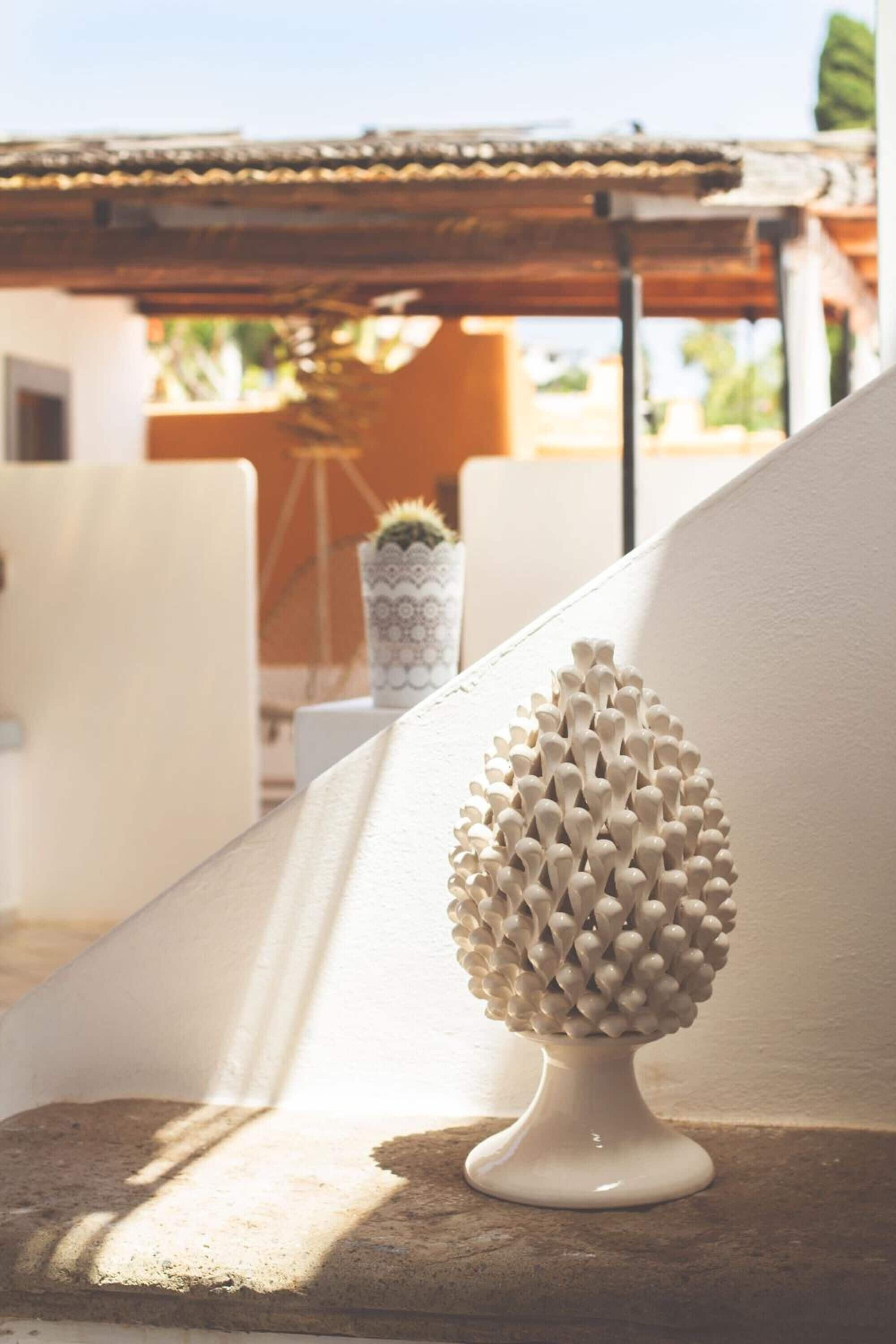 A white, textured sculpture on a balcony with a view of a building and a potted plant in the background.