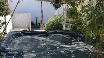 Ein Whirlpool mit strukturierter Oberfläche, umgeben von Bambuspflanzen und einer Pergola.