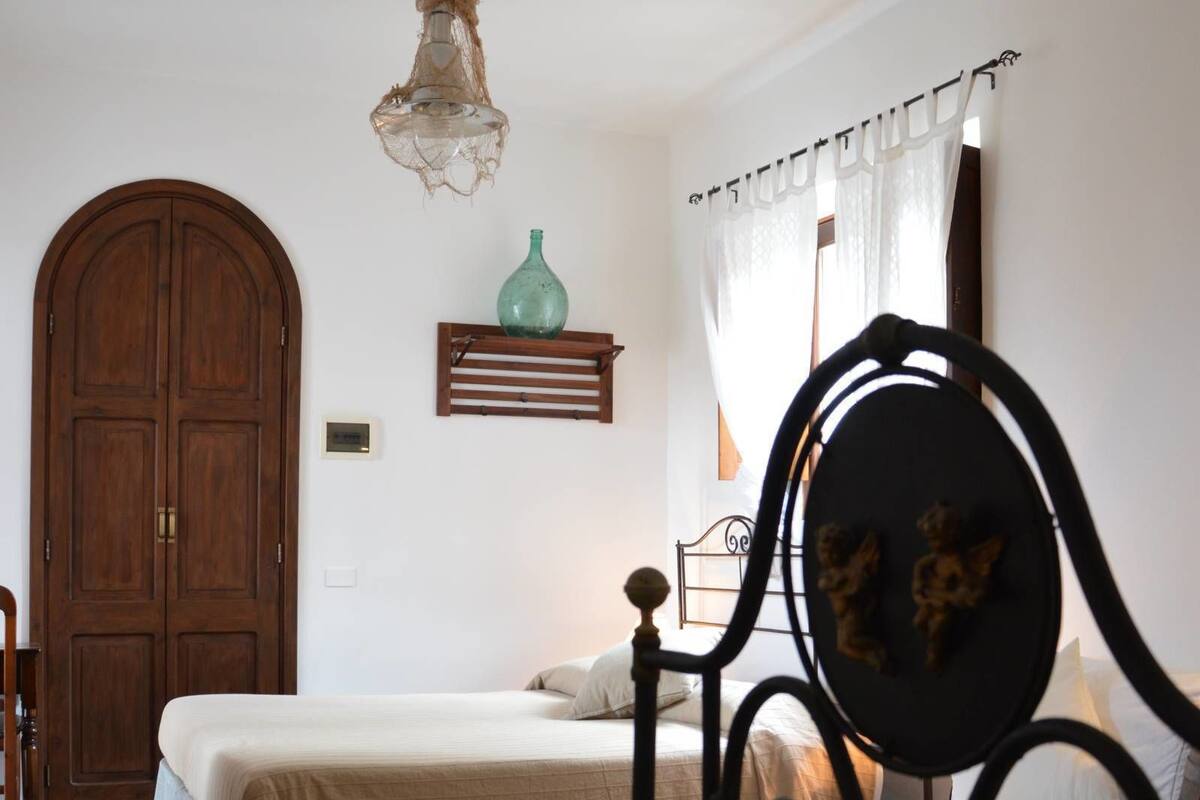 A bedroom with a bed, a wooden wardrobe, a hanging light fixture, and a metal headboard.