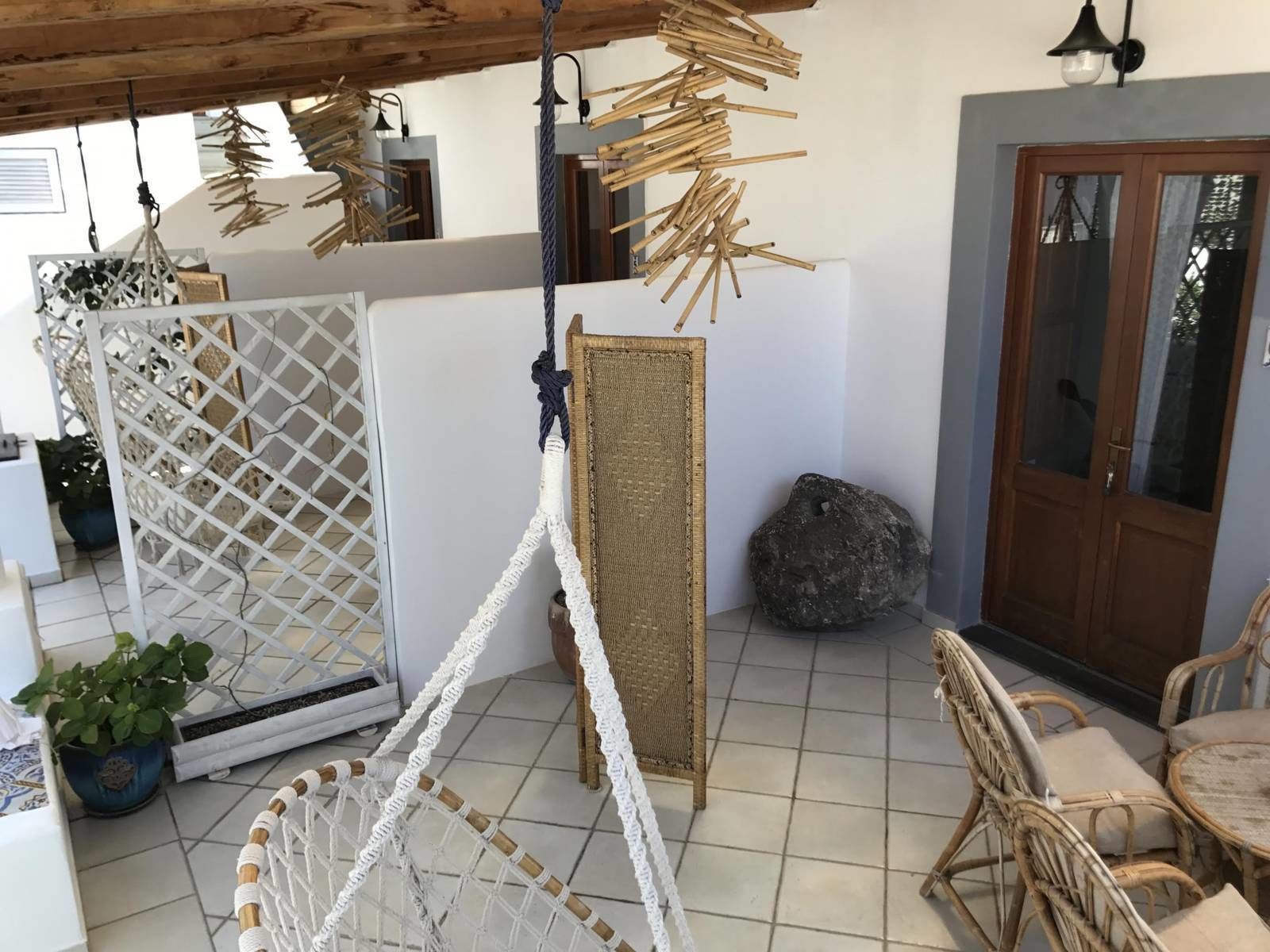 Una habitación con una hamaca, muebles de mimbre, un separador de celosía blanca y piedra.