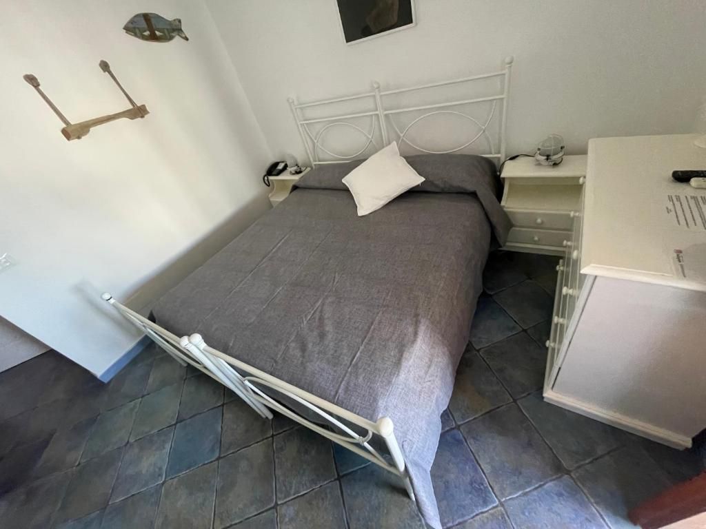 A bed with a metal frame, a bedside table with a lamp, and a small shelf with a phone and a remote control.