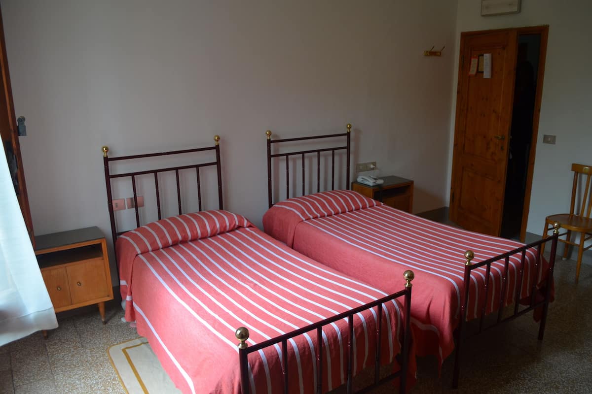A bedroom with two single beds, a wooden nightstand, a bedside table, and a door.