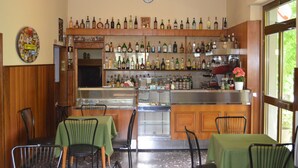 A bar area with wooden shelves stocked with various bottles, a clock on the wall, and a window with a view of greenery. - Albergo Padellino (Vaglia)