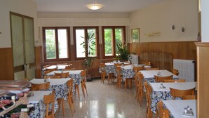 A dining area with multiple tables and chairs, wooden paneling on the walls, and large windows with views of greenery. - Albergo Padellino (Vaglia)