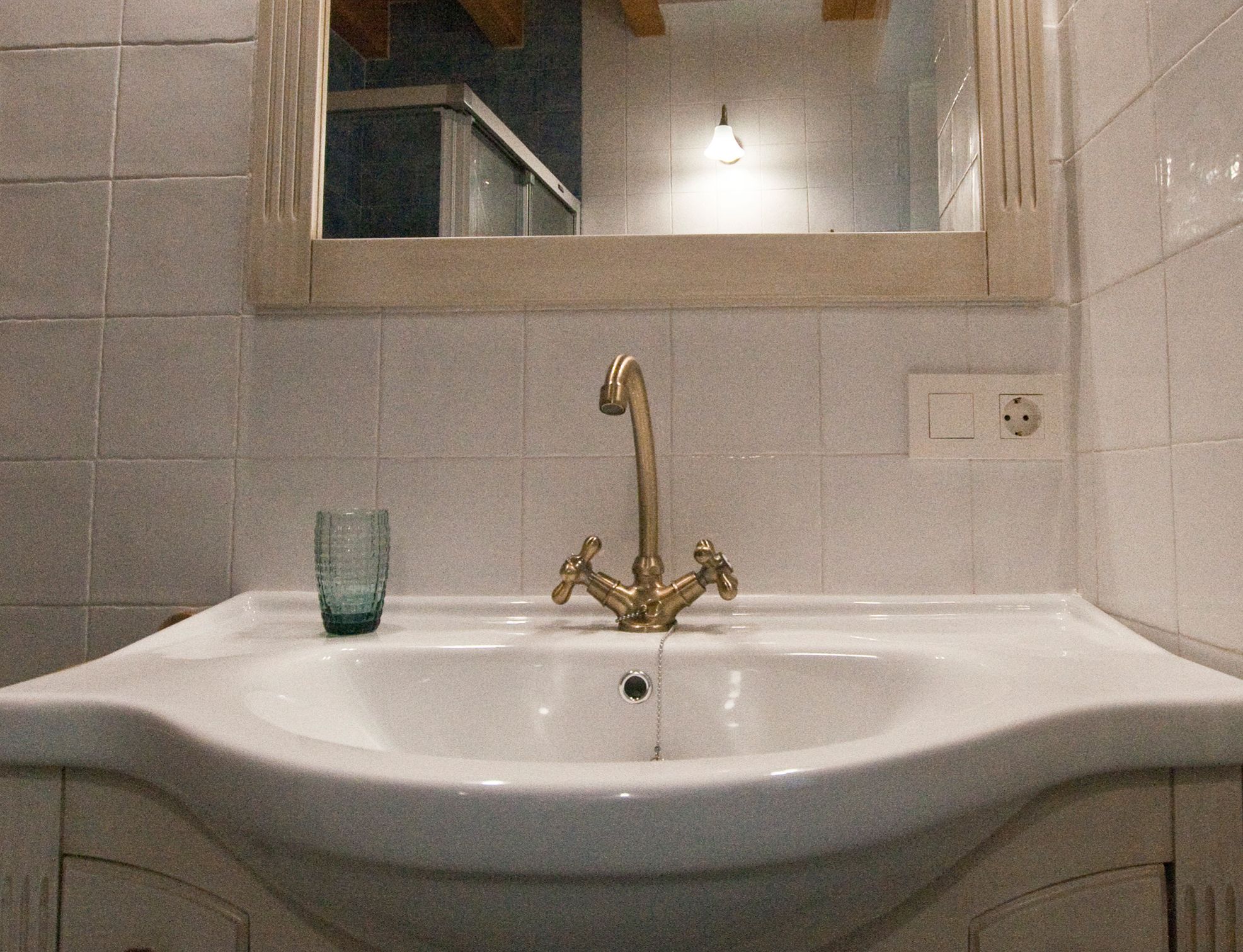 Ein Badezimmer mit einem weißen Waschbecken, einem goldenen Wasserhahn und einer blauen Glasablage.