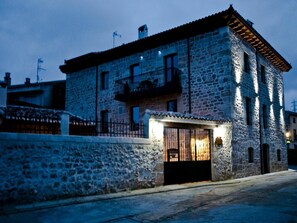 Un edificio de piedra con un balcón, un pequeño porche con una silla y una reja.