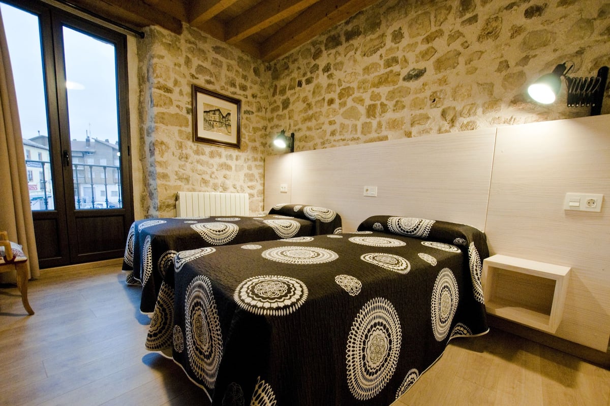 Een slaapkamer met twee bedden, een stenen muur, een lijst met een afbeelding en een raam met uitzicht.