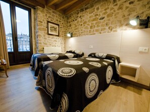 Un dormitorio con dos camas, una pared de piedra, un cuadro enmarcado y una ventana con vistas.