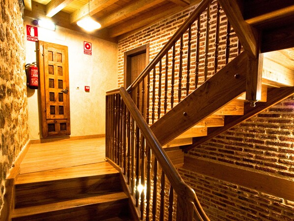 A wooden staircase with a brick wall background, a wooden door, and a fire extinguisher on the wall.