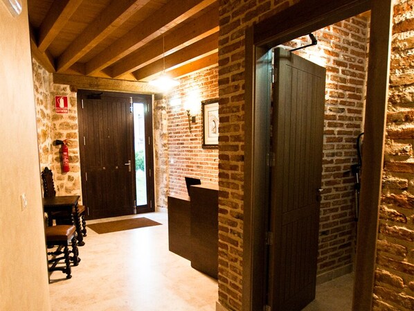 A hallway with stone walls and wooden beams, a fire extinguisher, and a bench.