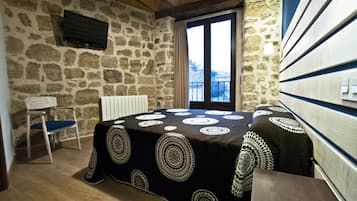 Un cuarto acogedor con pared de piedra, techo de madera, cama con colcha estampada, una silla y ventana con vista a un paisaje nevado.