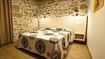 Een slaapkamer met een stenen muur, een bed met beddengoed met een patroon, een nachtkastje en een wandlamp.