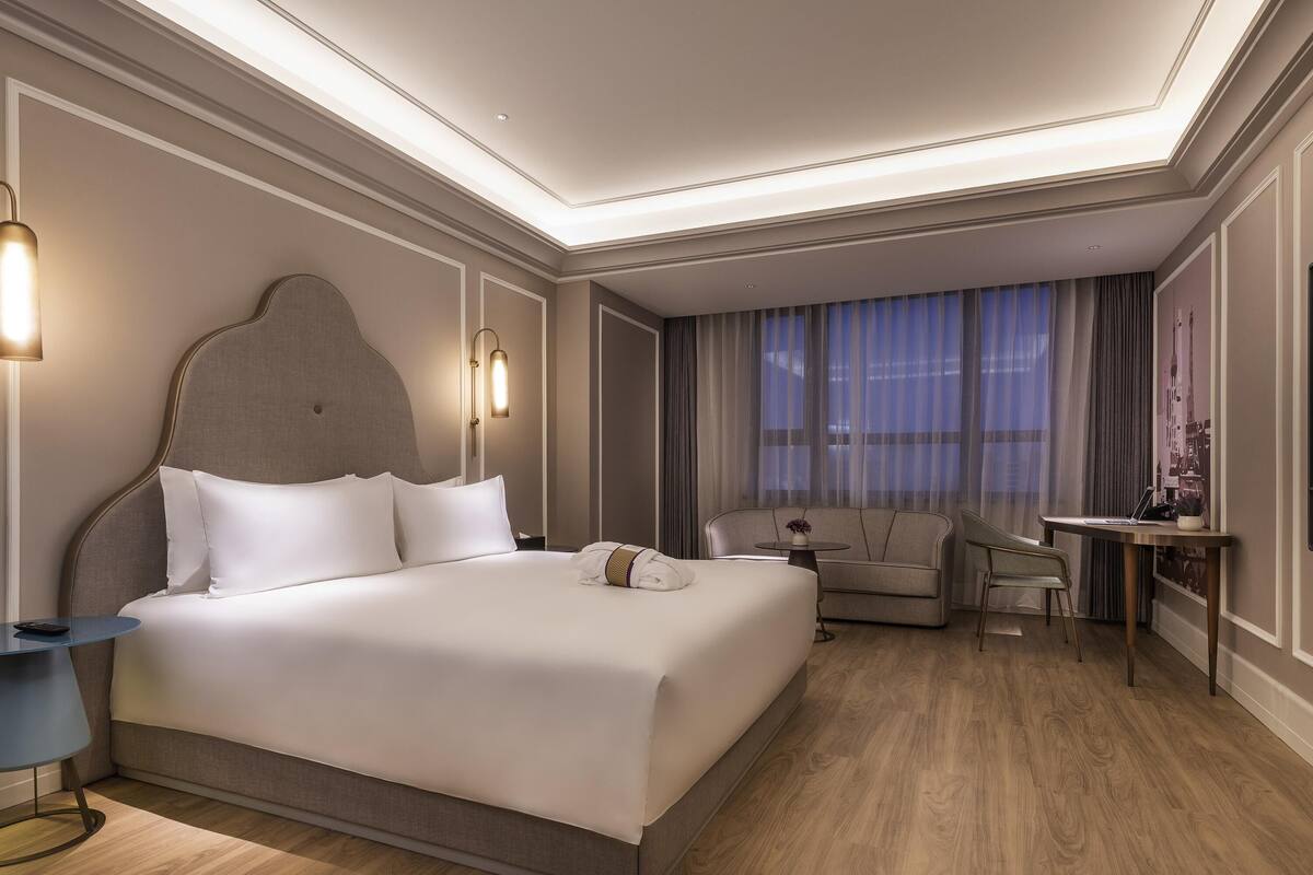 Ein Hotelzimmer mit einem großen Bett, einer Couch, einem Schreibtisch und einem Fenster mit Vorhängen.