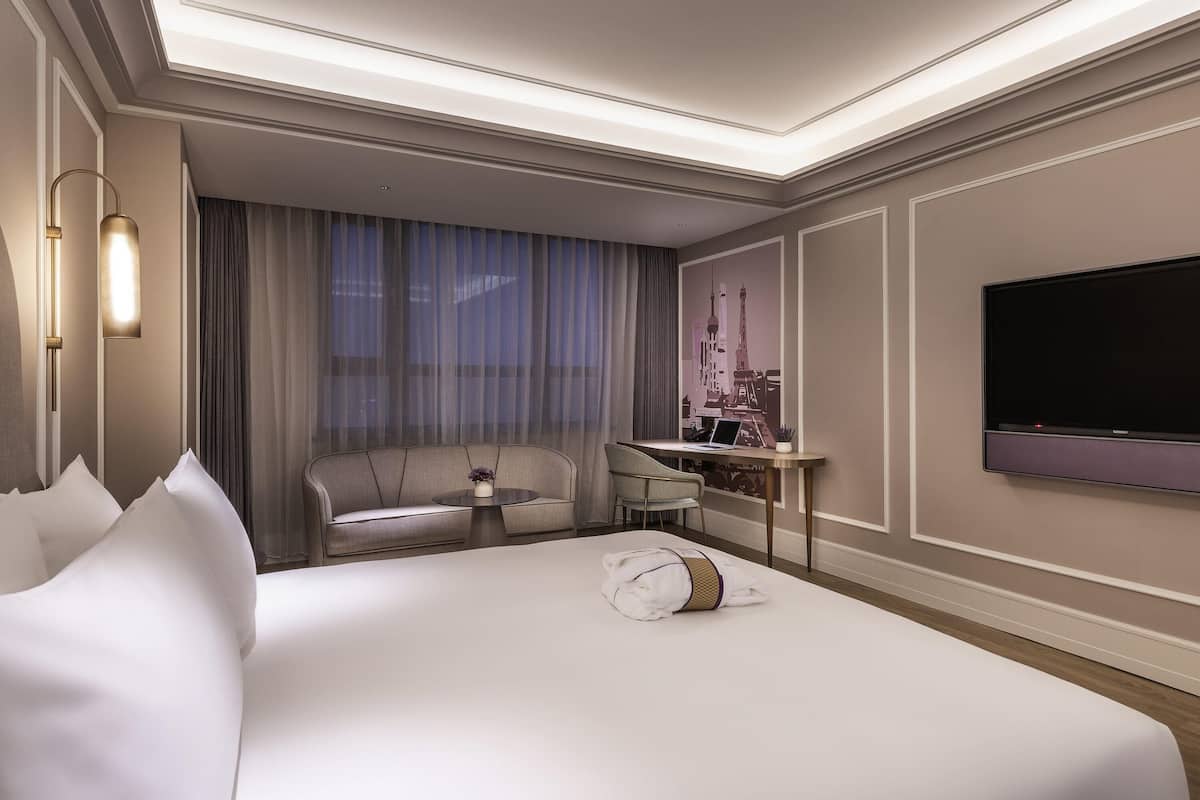 Habitación de hotel con una cama grande, un escritorio con una laptop, un televisor y vista del paisaje urbano a través de la ventana.