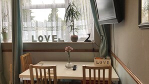 A dining area with a table, chairs, a potted plant, and a TV mounted on the wall. - Love & Peace (Orpington)