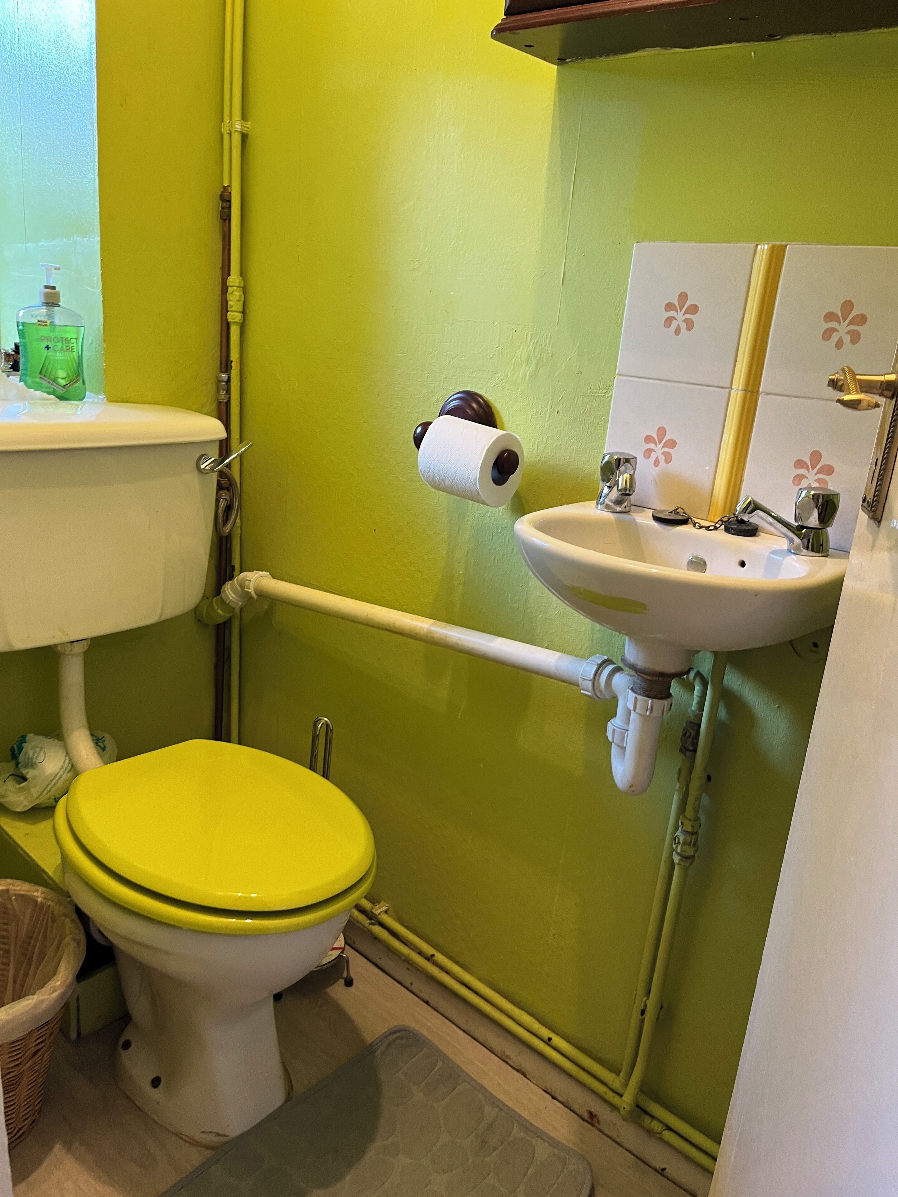 A bathroom with a yellow toilet, a white sink, and green walls.