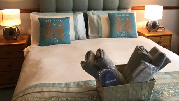 A hotel room with a large bed, grey upholstered headboard, and two bedside lamps. - Love & Peace (Orpington)