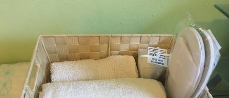 A wicker basket with a tag labeled "Bathing Suit" containing a white towel.