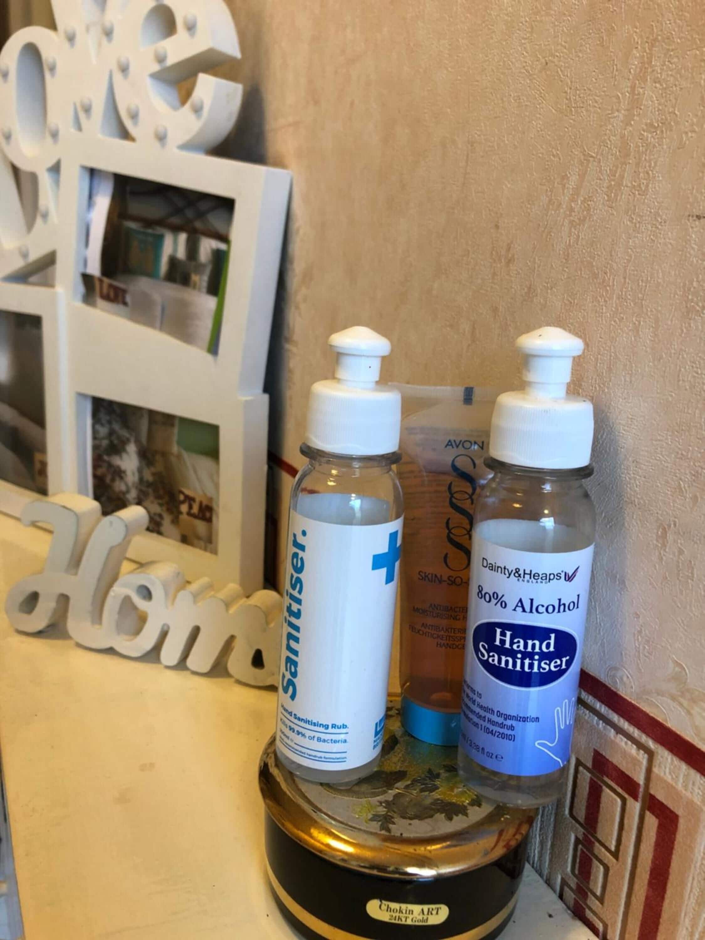 Dos botellas de gel antibacterial y un objeto decorativo con la palabra 'Home' sobre una mesa.