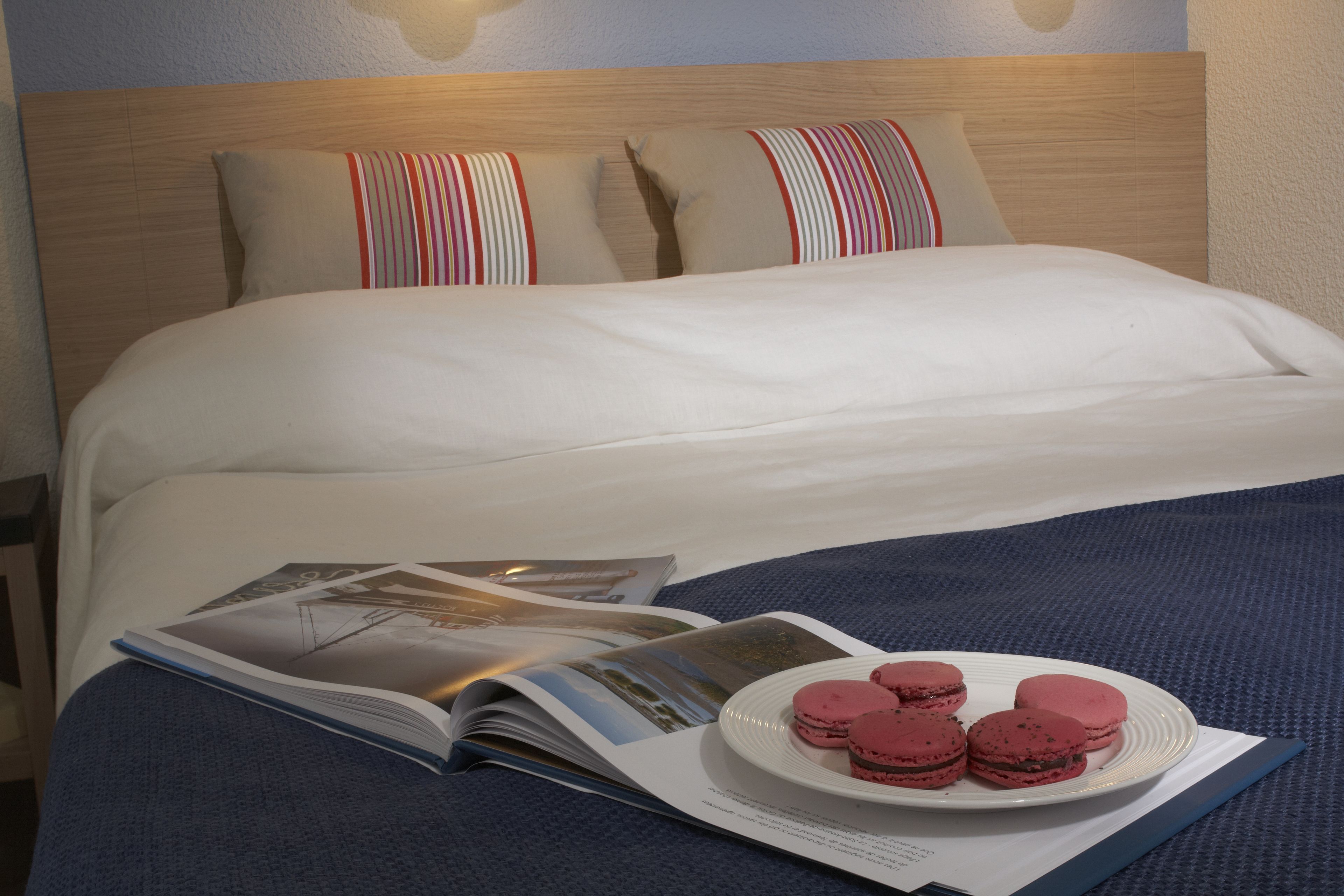 Un lit bien fait, avec un magazine et une assiette de macarons.