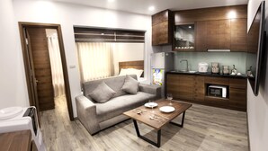 A modern living room with a sofa, a coffee table, and a kitchen area with wooden cabinets and appliances. - iRest Apartment (Hanoi)