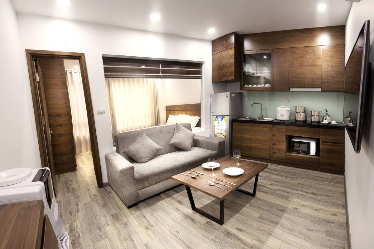 A modern living room with a sofa, a coffee table, and a kitchen area with wooden cabinets and appliances.