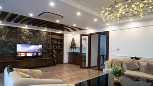 A modern living room with a flat-screen TV, wooden shelving, a Christmas tree, and a glass coffee table. - iRest Apartment (Hanoi)