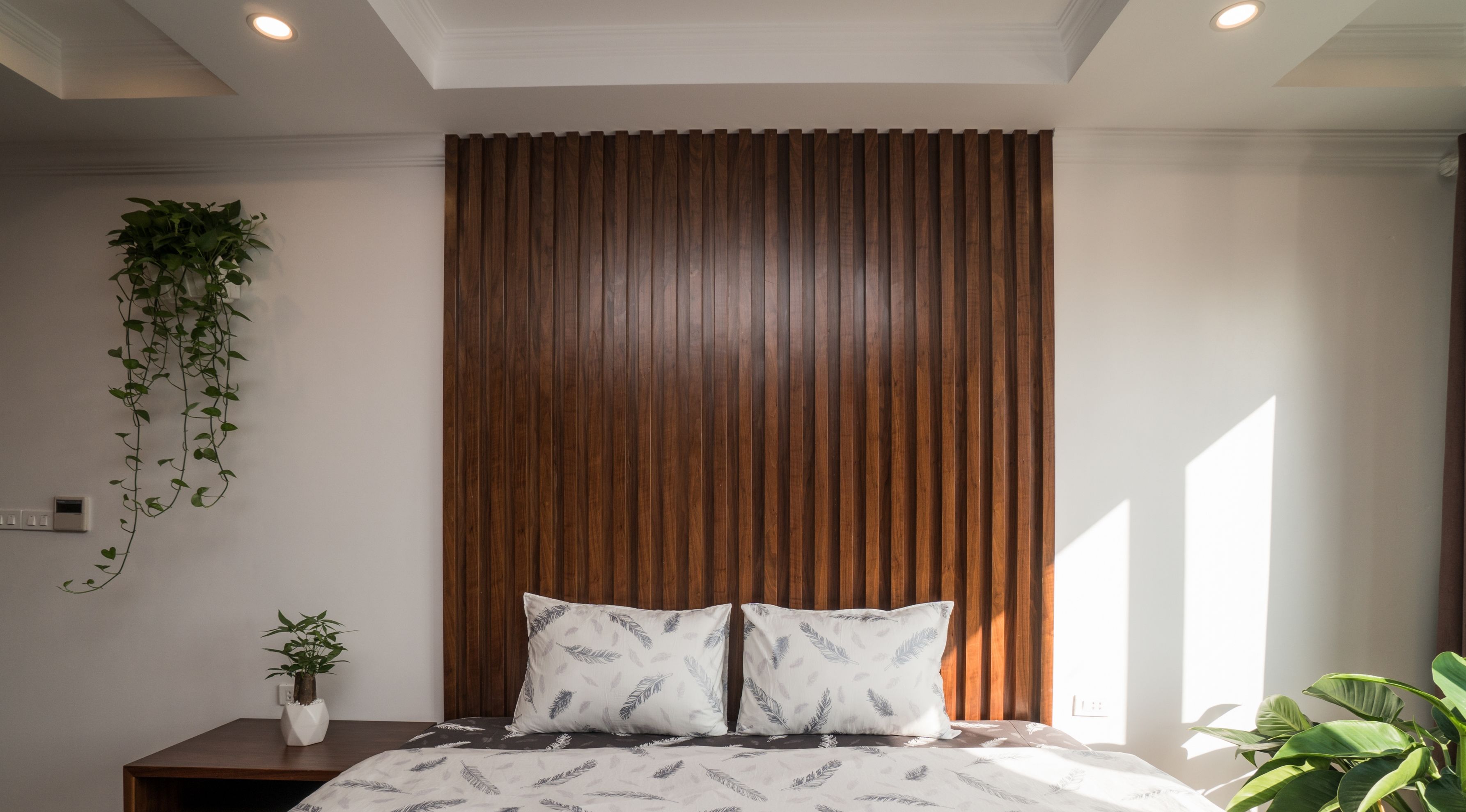 A bedroom with a wooden headboard, a bed with patterned bedding, a bedside plant, and a hanging plant.