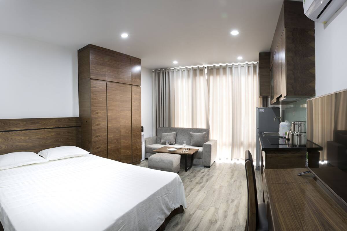 A hotel room with a bed, a sofa, a desk, a television, and a kitchenette.