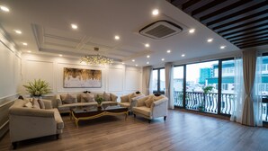 A spacious living room with a large sofa set, a coffee table, and a chandelier. There is a large window with a view of the city. - iRest Apartment (Hanoi)
