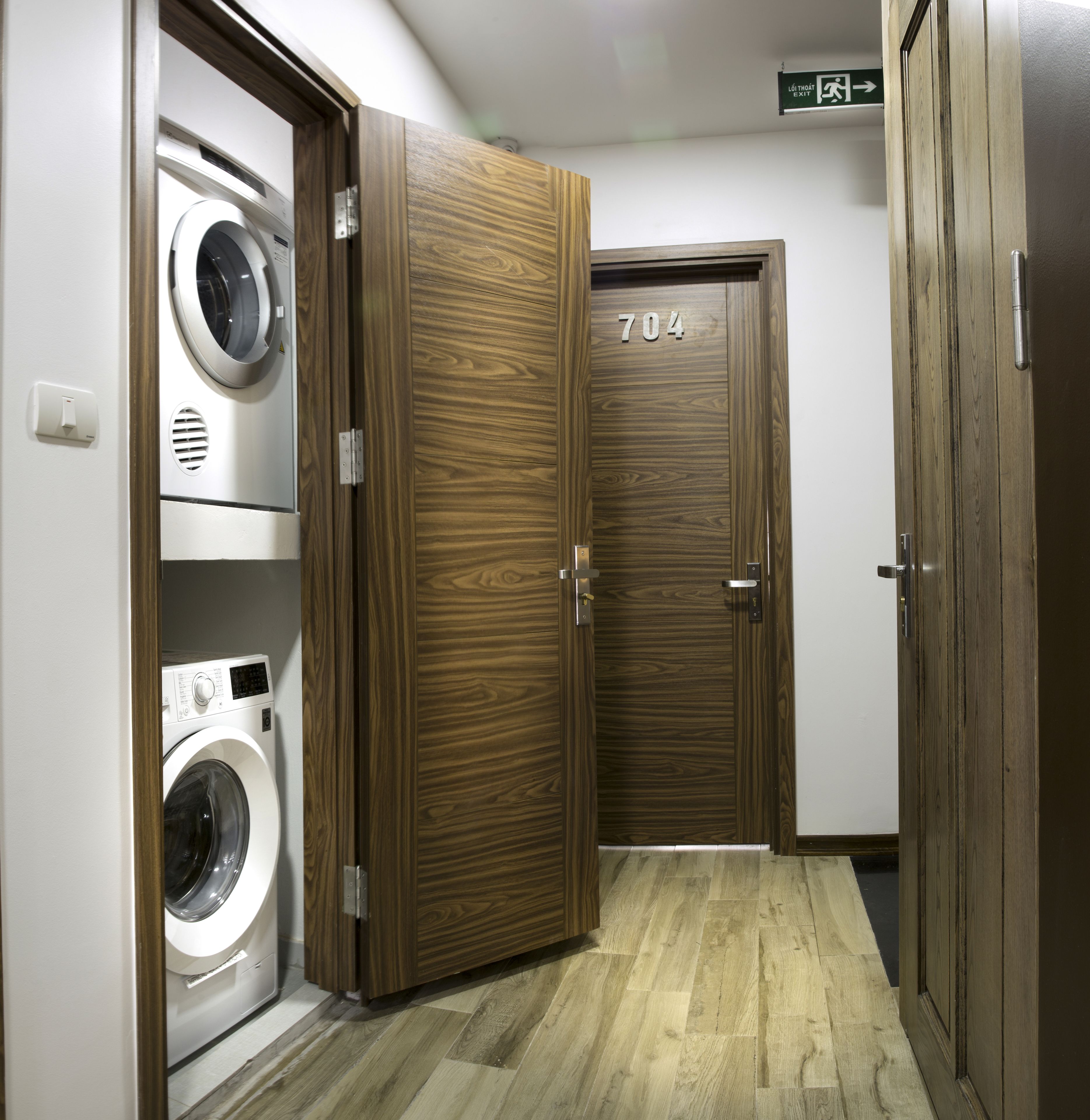 A laundry room with a washing machine and dryer, a wooden door with the number 704, and a sign indicating the exit direction.