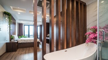 Quarto moderno com cama grande, divisória de madeira e banheiro com banheira e flores cor-de-rosa.